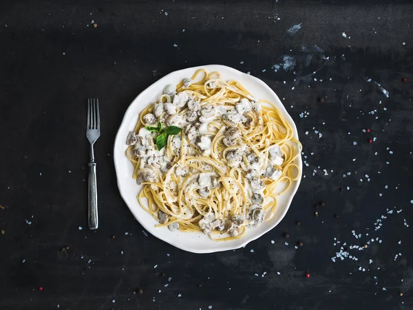 Pasta-Spaghetti mit cremiger Pilzsoße und Basilikum in weißem Keramikteller über altem Grunge-Tisch — Stockfoto