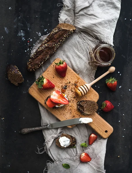 Colazione pronta. Crostini alla baguette nera con fragole fresche, miele e mascarpone sulla superficie scura della tavola grunge — Foto Stock