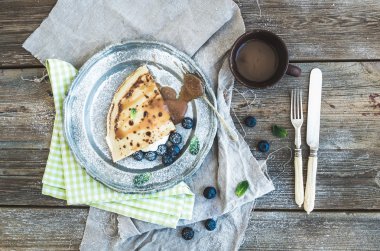 İnce gözleme veya taze yaban mersini, krem, nane ve rustik ahşap zemin üzerinde vintage metal plaka tuzlu karamel soslu krep