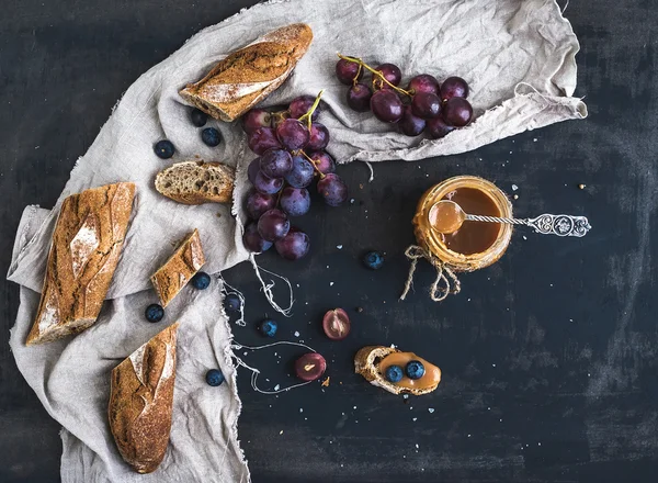 Francouzské bagety nakrájíme na kousky, červené hrozny, borůvky a sůl karamelem na rustikální tmavé pozadí — Stock fotografie