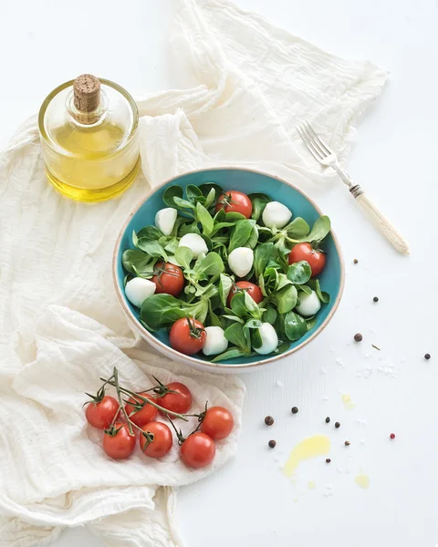 Salada de primavera com cordeiros alface, mussarela e tomate cereja em tigela de cerâmica azul sobre fundo branco — Fotografia de Stock