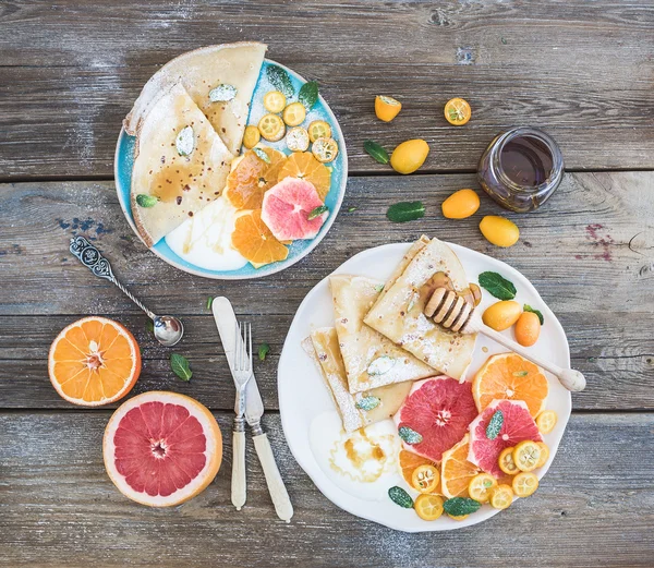 Conjunto de café da manhã primavera vitamina. Crepes finos ou panquecas com toranja fresca, laranja, kumquat, mel, creme e folhas de hortelã sobre um fundo de madeira rústica — Fotografia de Stock