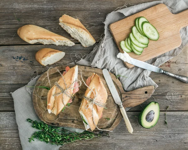 Panini di salmone, avocado e timo in baguette legati con corda decorativa su una tavola di legno rustico su fondo di legno grezzo — Foto Stock