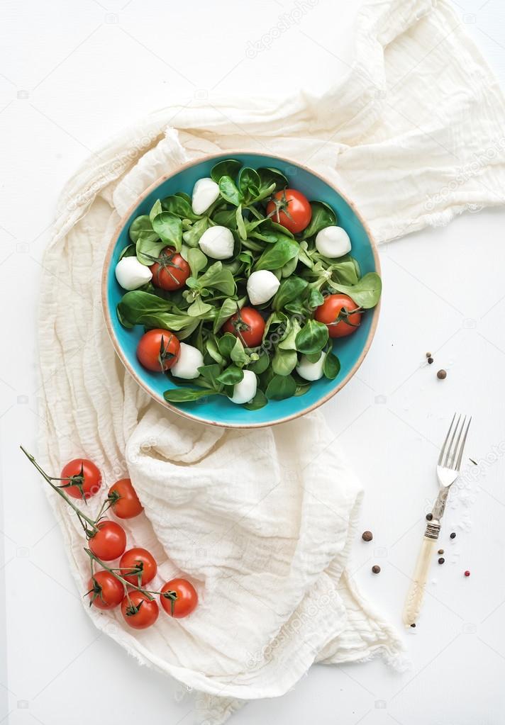 Spring salad with lambs lettuce, mozarella and cherry-tomatoes in blue ceramic bowl over white backdrop