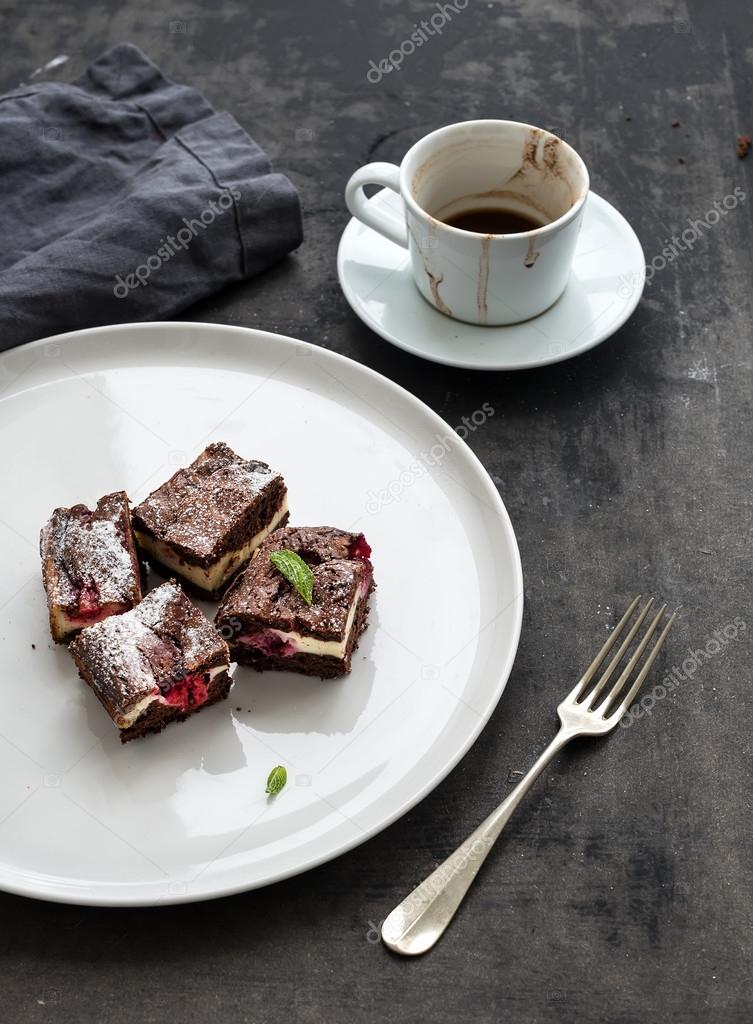 Cheesecake brownie squares with raspberries and coffee on white ceramic plate over dark grunge table surface