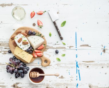 Peynir meze seçimi veya şarap aperatif küme. Peynir, üzüm, pekan fındık, çilek ve bal rustik beyaz zemin, üstten görünüm üzerinde yuvarlak ahşap tahta üzerinde çeşitli