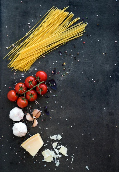Marco alimenticio. Pasta ingredientes. Tomates cereza, pasta de espaguetis, ajo, albahaca, parmesano y especias sobre fondo grunge oscuro, espacio para copiar —  Fotos de Stock