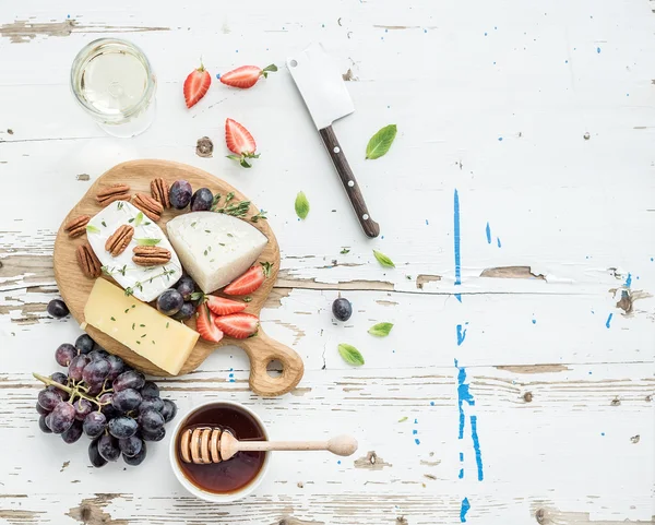 Peynir meze seçimi veya şarap aperatif küme. Peynir, üzüm, pekan fındık, çilek ve bal rustik beyaz zemin, üstten görünüm üzerinde yuvarlak ahşap tahta üzerinde çeşitli
