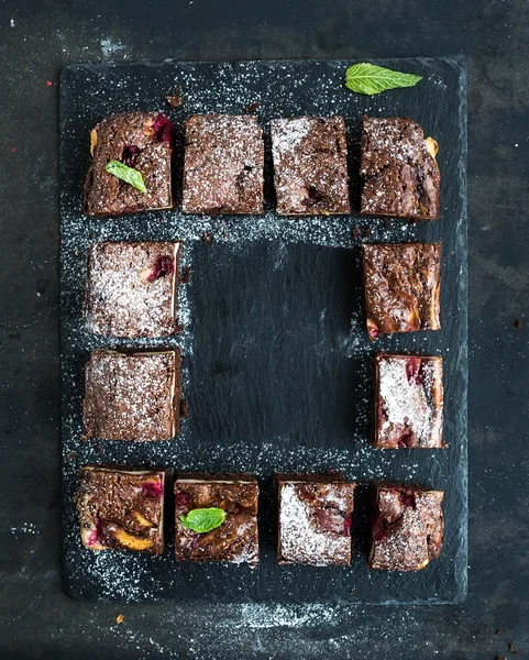 Schokoladen- und Himbeer-Brownie-Quadrate auf schwarzem Steinbrett vor dunkler Grunge-Kulisse — Stockfoto