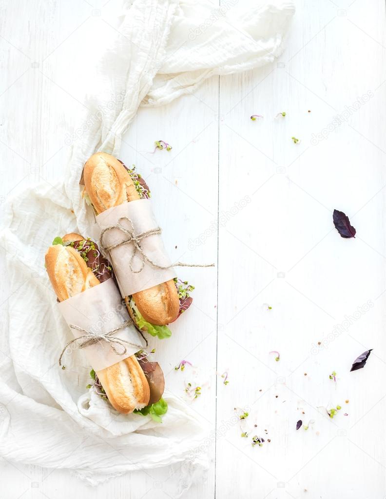 Sandwiches with beef, fresh vegetables and herbs over white wood backdrop, copy space