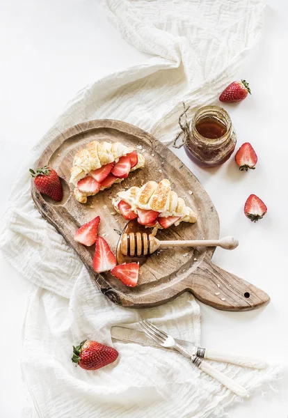 Свіжоспечені круасани з полуницею, маскарпоном та медом на сільській дерев'яній дошці на білому тлі — стокове фото