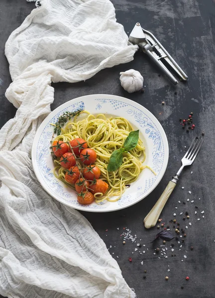 Makaron spaghetti z sosem pesto, bazylia, pieczone pomidory na rustykalne tabke drewniany ciemny tabela, widok z góry — Zdjęcie stockowe