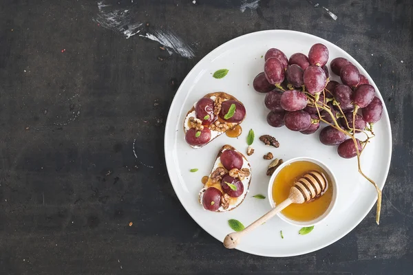 Kahvaltı Seti. ricotta peyniri, üzüm, ceviz ve ballı karanlık grunge yüzey üzerinde beyaz seramik plaka üzerinde tatlı sandviç — Stok fotoğraf