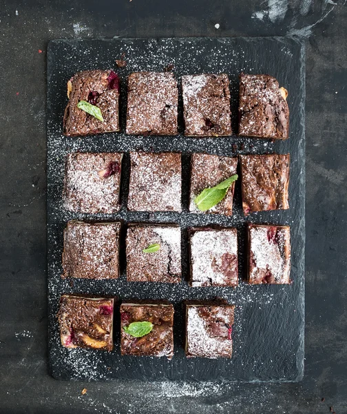 Schokoladen- und Himbeer-Brownie-Quadrate auf schwarzem Steinbrett vor dunkler Grunge-Kulisse — Stockfoto