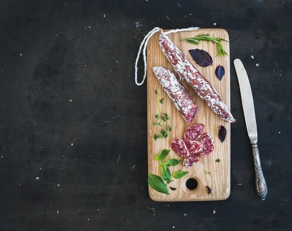 Snack gourmet de carne. Salami, ajo y hierbas sobre tabla rústica de madera sobre fondo grunge oscuro —  Fotos de Stock