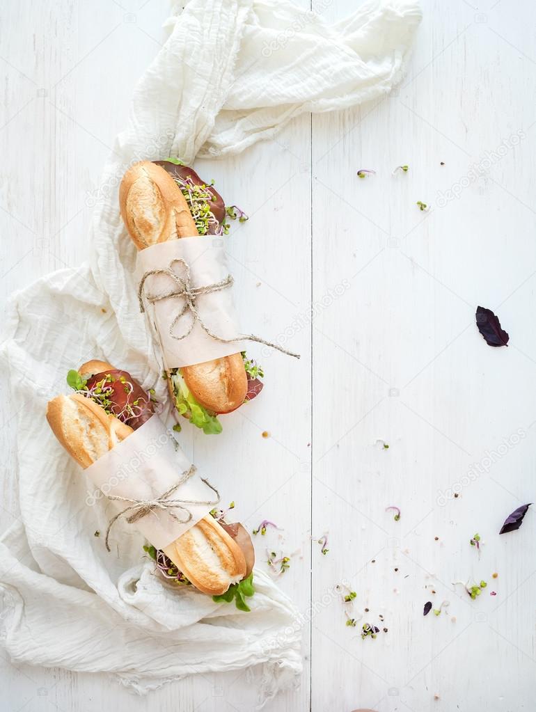 Sandwiches with beef, fresh vegetables and herbs over white wood backdrop, copy space