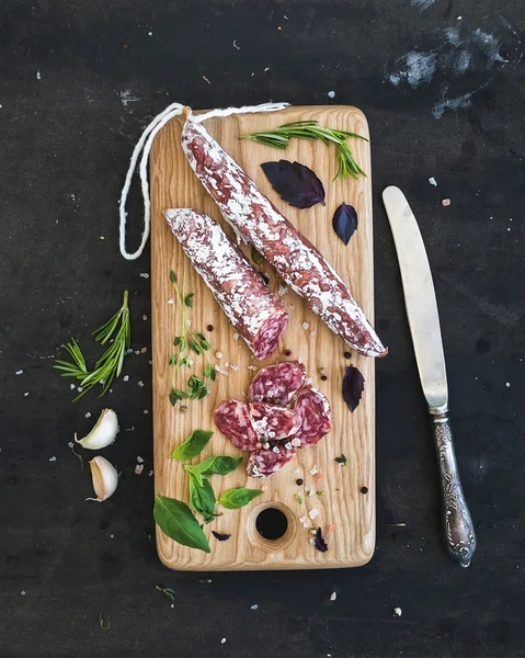 Snack gourmet de carne. Salami, ajo y hierbas sobre tabla rústica de madera sobre fondo grunge oscuro —  Fotos de Stock