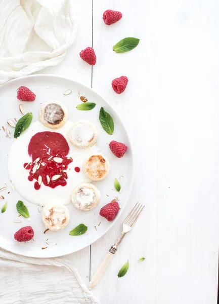 Rustic breakfast set. Russian cottage cheese cakes on ceramic plate with berry jam, almonds, fresh raspberries and mint over white wooden backdrop, top view — Stock Photo, Image