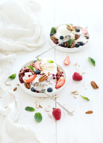 Healthy breakfast. Berry crumble with fresh blueberries, raspberries, strawberries, almond, walnuts, pecans, yogurt, and mint in ceramic plates over white wooden surface — Stock Photo, Image