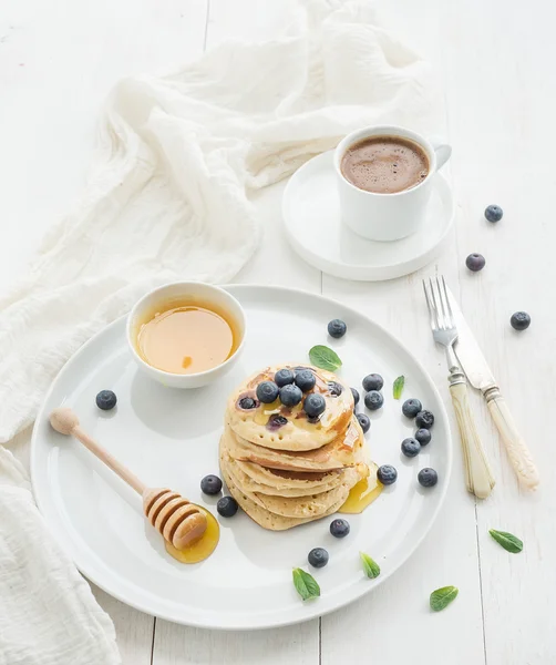 Reggeliző készlet. áfonyás palacsinta friss bogyós gyümölcsök, a méz, a menta leveleket és a csésze kávé fölött fehér fa háttér — Stock Fotó