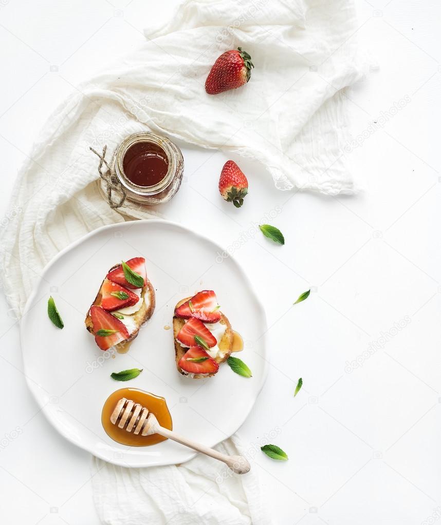 French toasts with strawberry, cream cheese, honey and mint on light ceramic plate over white backdrop