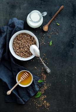 Rustik sağlıklı kahvaltı seti. Karabuğday kabuğu çıkarılmış tane süt ve bal karanlık grunge zemin üzerinde ile pişmiş