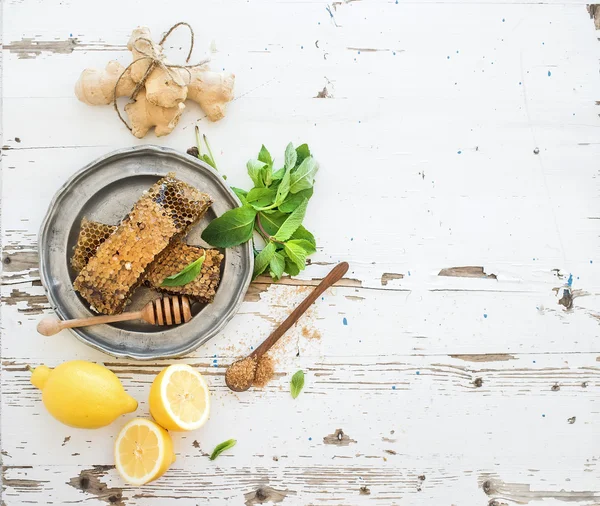 Herbal tea cooking set. Fresh mint, honeycombs, lemon, ginger on rustic white wooden background. Top view