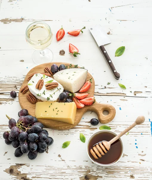 Käsevorspeise oder Wein-Snack-Set. Käsesorten, Trauben, Pekannüsse, Erdbeeren und Honig auf rundem Holzbrett vor rustikalem weißen Hintergrund — Stockfoto