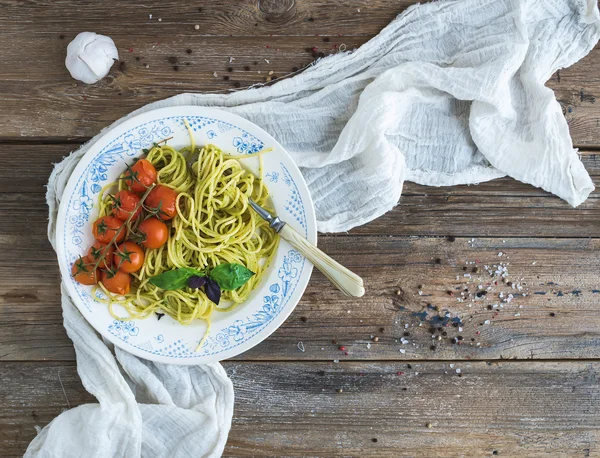 Pasta spaghetti with pesto sauce, basil, garlic, baked cherry-tomatoes on rustic wooden table, top view — Stock fotografie