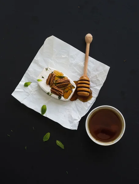 Formaggio Camembert con noci pecan, menta e miele su carta da imballaggio su sfondo nero, vista dall'alto — Foto Stock