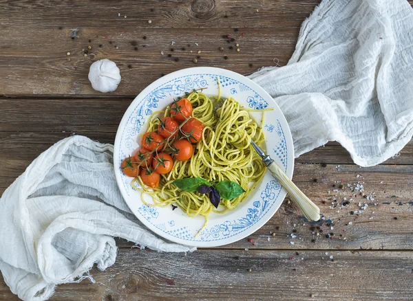 Pasta spaghetti with pesto sauce, basil, garlic, baked cherry-tomatoes on rustic wooden table, top view — Zdjęcie stockowe