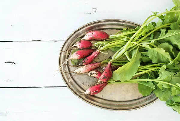 Bunch of fresh dirty garden radishes on vintage metal tray over rustic white wooden backdrop, top view — Stock Fotó