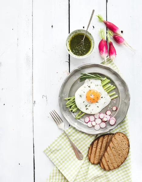 Healthy breakfast set. Fried egg with asparagus, radishes, green sauce and bread on vintage metal plate over white wooden backdrop, top view — Φωτογραφία Αρχείου