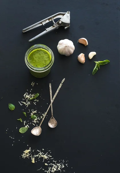 Jar of fresh home made pesto with ingredients for it. Fresh basil leaves, grated parmesan cheese and garlic over black backdrop. Top view — Zdjęcie stockowe