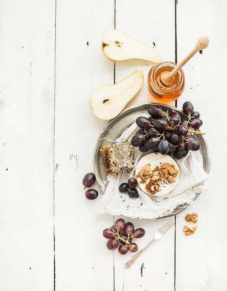 Ser Camembert z winogron, orzechy włoskie, gruszka i miód na vintage blachy na białym tle rustykalnym drewna, widok z góry — Zdjęcie stockowe