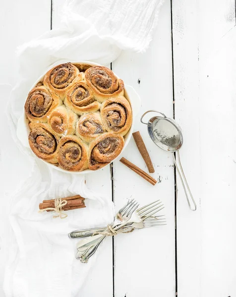 Petits pains à la cannelle fraîchement cuits dans un plat sur une table en bois rustique, vue sur le dessus — Photo