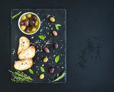 Akdeniz zeytin otlar ve karanlık grunge arka plan, üstten görünüm üzerinde siyah arduvaz tepsi ciabatta dilimleri ile