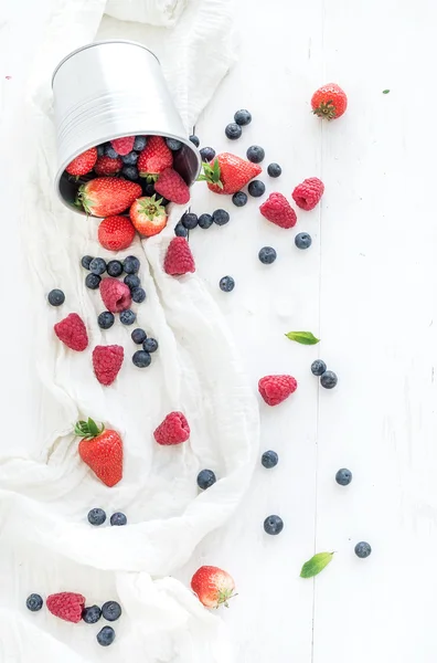 Berry frame with copy space on right. Metal bucket, strawberries, raspberries, blueberries and mint leaves, white wooden background, top view — Stock Photo, Image