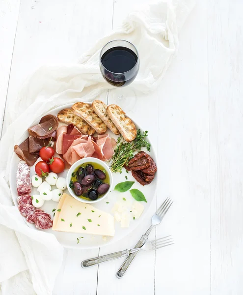 Set de aperitivos de vino. Tomates cereza, queso parmesano, variedad de carne, rebanadas de pan, tomates secos, aceitunas y albahaca en plato de cerámica redonda sobre fondo de madera blanca — Foto de Stock