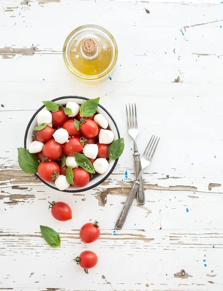 Ensalada Caprese: tomates cherry y mozzarella en cuenco de metal con aceite de oliva sobre fondo rústico de madera blanca, vista superior , —  Fotos de Stock