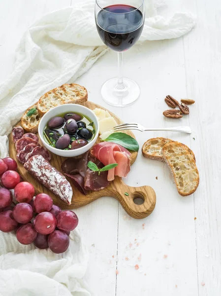 Conjunto de aperitivos de vinho. Copo de tinto, uvas, queijo parmesão, variedade de carne, fatias de pão, nozes de nozes, mel, azeitonas e manjericão em tábua de madeira rústica sobre fundo branco — Fotografia de Stock