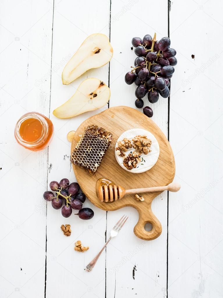 Camembert cheese with grape, walnuts, pear and honey on oak serving board over white rustic wood backdrop, top view