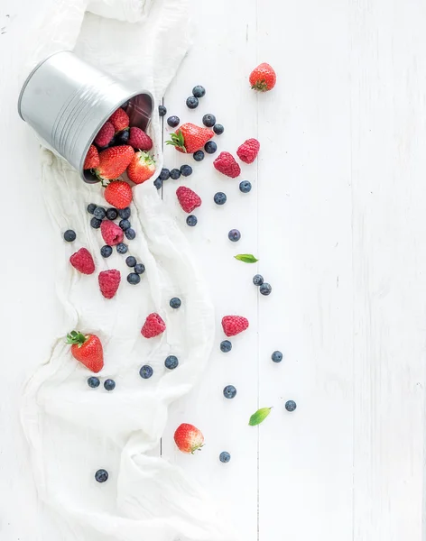 Berry frame with copy space on right. Metal bucket, strawberries, raspberries, blueberries and mint leaves, white wooden background, top view — Stock Photo, Image