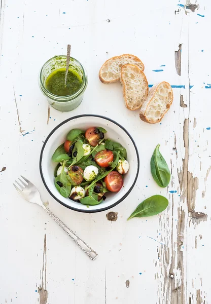 Salát Caprese, chiabatta plátky. Cherry rajčata, baby špenátem a mozzarellou v kovové misce s pesto přelivem na rustikální dřevěné bílé pozadí — Stock fotografie