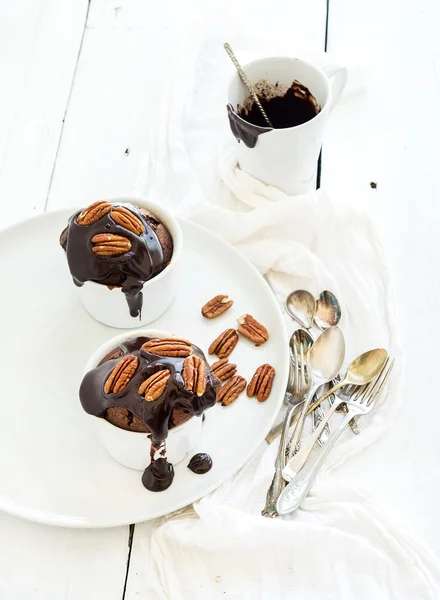 Sabrosas magdalenas marrones caseras con glaseado de ganache de chocolate y nueces de pacana en tazas de panadería separadas . —  Fotos de Stock