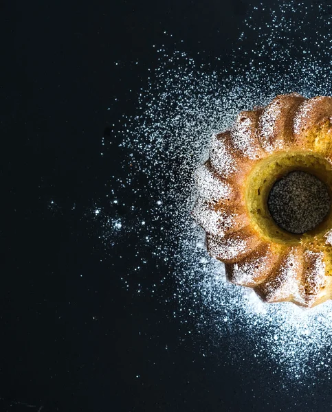 Moist orange bundt yoghurt cake with sugar powder on top, dark grunge background.