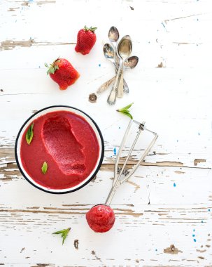 Strawberry sorbet or ice-cream with fresh berries, mint and metal scooper on over white rustic wooden backdrop, top view