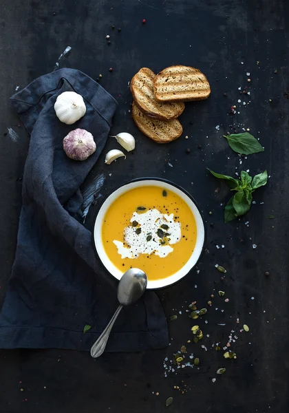 Тыквенный суп со сливками, семенами, хлебом и свежим базиликом на гранжевом черном фоне — стоковое фото
