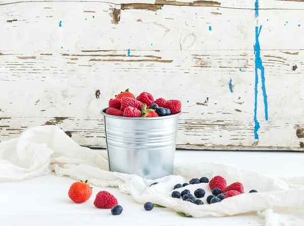 Cubo de metal de fresas, frambuesas, arándanos y hojas de menta, fondo de madera blanca — Foto de Stock