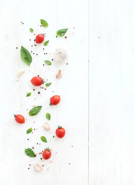 Cherry tomatoes, fresh basil leaves, garlic cloves and spices on rustic white wooden backdrop, top view